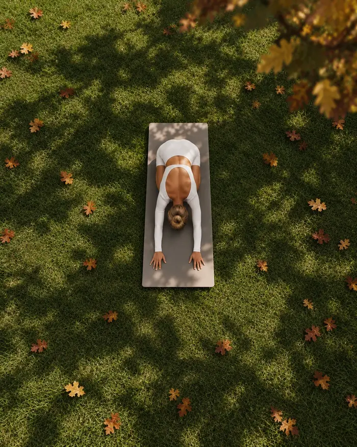 Posture de yoga en flexion avant sur un tapis, dans les feuilles d'automne